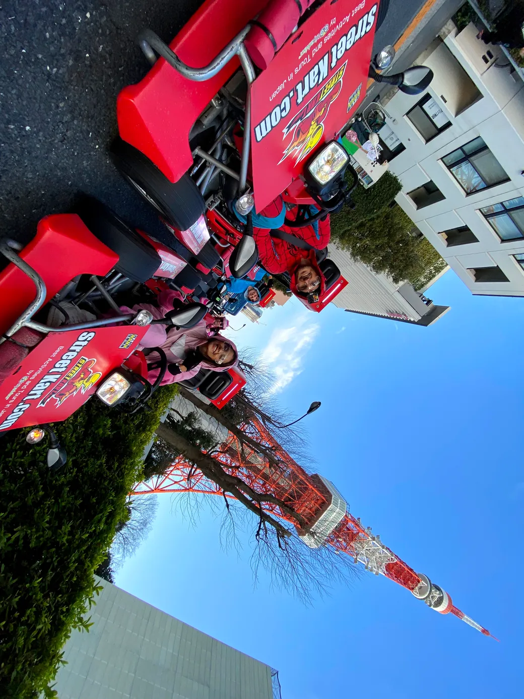 Group of people riding red promotional scooters lined up on a street with Tokyo Tower visible in the background